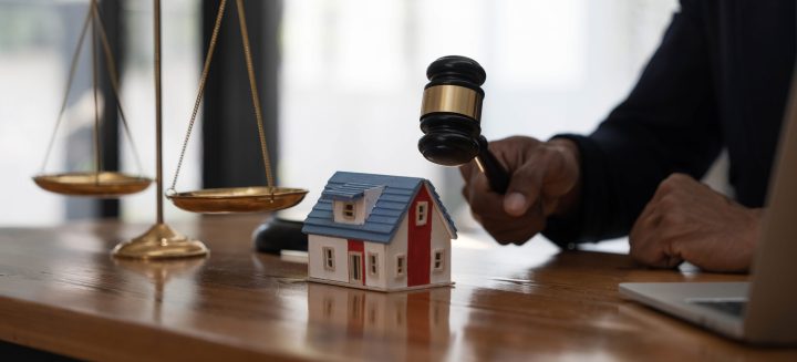 Close-up of a house in front of a lawyer holding a hammer and a laptop silver brass scales on a wooden table in his office, law, legal services, advice, justice and real estate ideas...