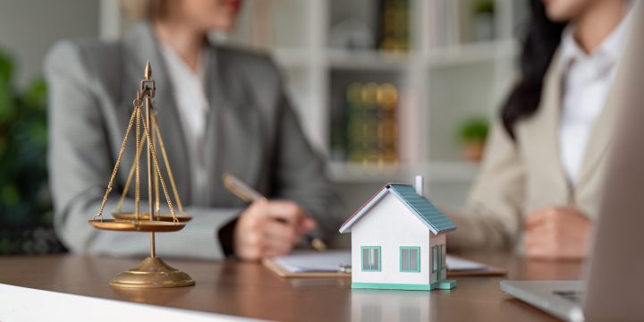 Two female lawyers of Asian descent discussing and reviewing real estate contract details in a modern office setting.